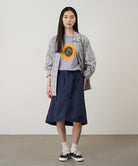 Person wearing a plaid shirt, graphic t-shirt, and navy skirt against a plain background