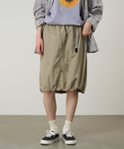 Person wearing a plaid shirt, gray top with sunflower design, beige skirt, and black sneakers on a plain background