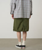 Person wearing a plaid shirt, green skirt, and black sneakers on a plain background
