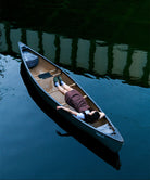 Woman wearing a brown Gramicci dress lying in a canoe on a calm body of water