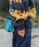 Gramicci teal ripstop chalk bag worn at the waist by a person wearing a yellow and black patterned mohair sweater and dark pants.   