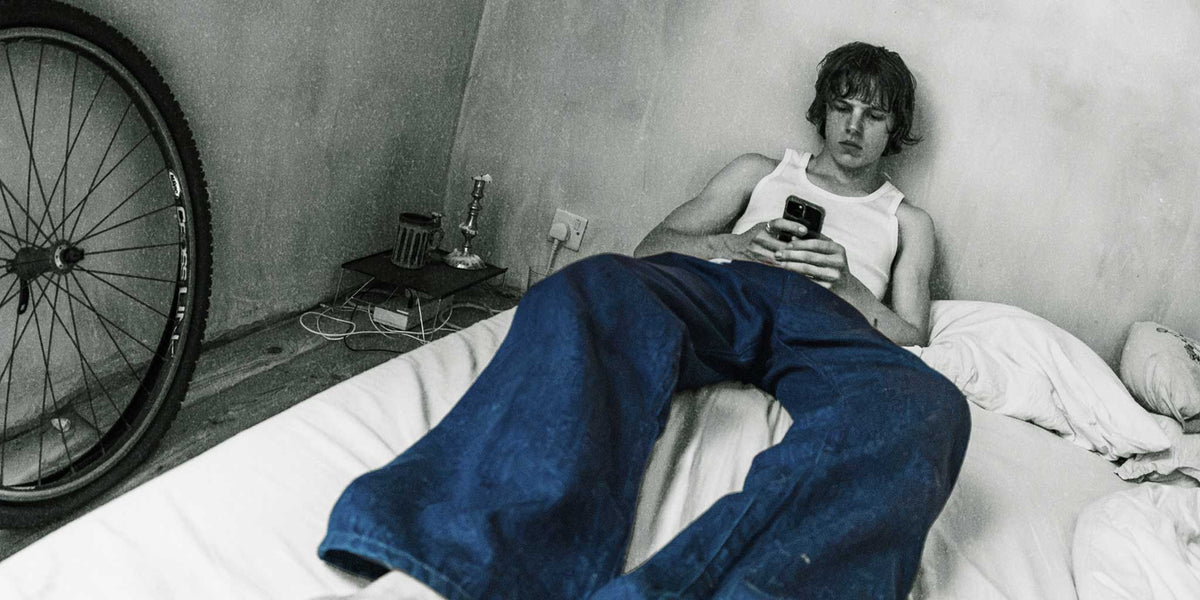 Gramicci relaxed blue denim jeans worn by a person lounging on a bed in a black-and-white room.