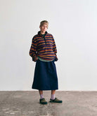 Model wearing a Gramicci multicolored striped fleece pullover, a navy midi skirt, a tan headband, lavender socks, and olive-green outdoor sandals.   