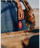 Person holding a red Hotel Keychain wearing blue jeans with a blurred background.