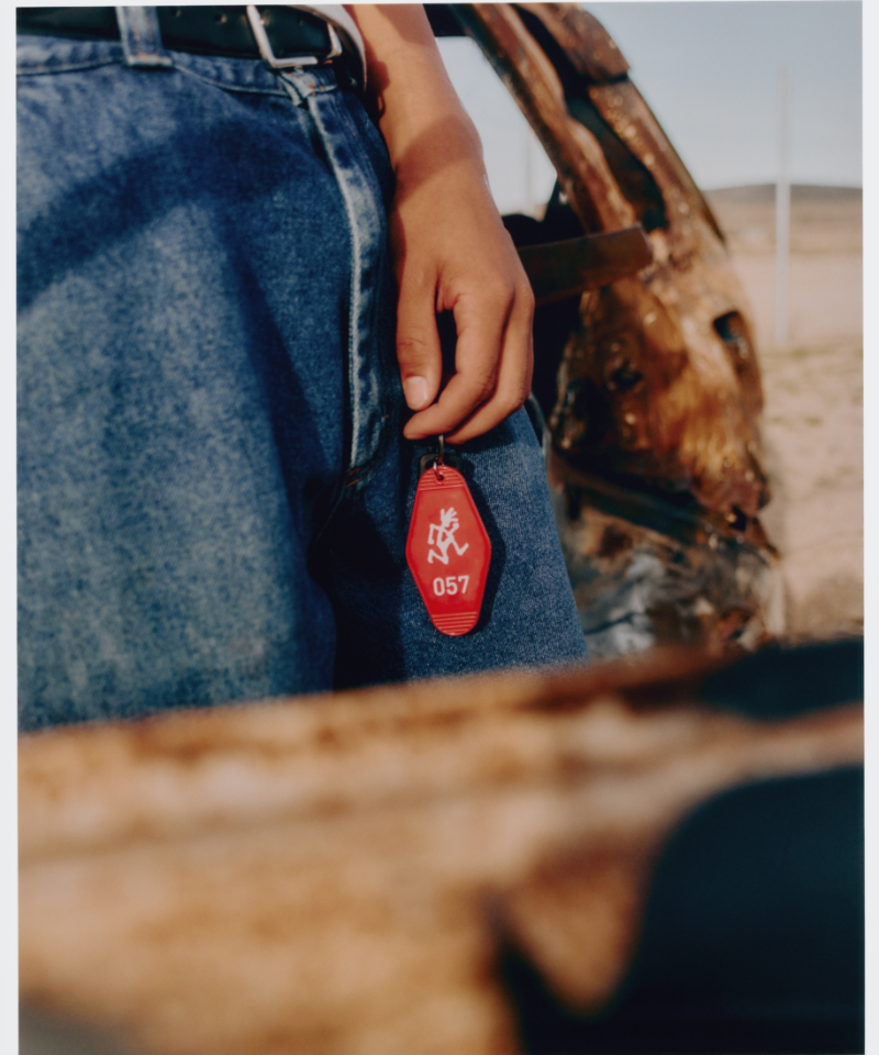 Person holding a red Hotel Keychain wearing blue jeans with a blurred background.