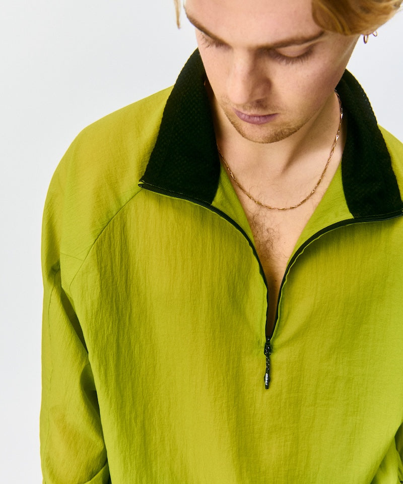 Model wearing a kiwi Gramicci Ultra-Light Packable Jacket with a black collar on a light-tone background.