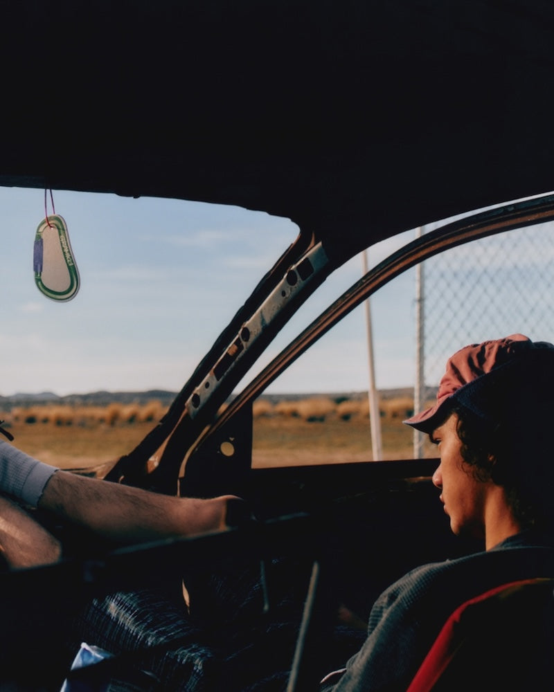 Two people sitting inside a car with a scenic view of a field and sky through the open window.