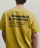 Back view of a model wearing a Gramicci yellow G-Sail Tee with black graphic against a light-tone background.