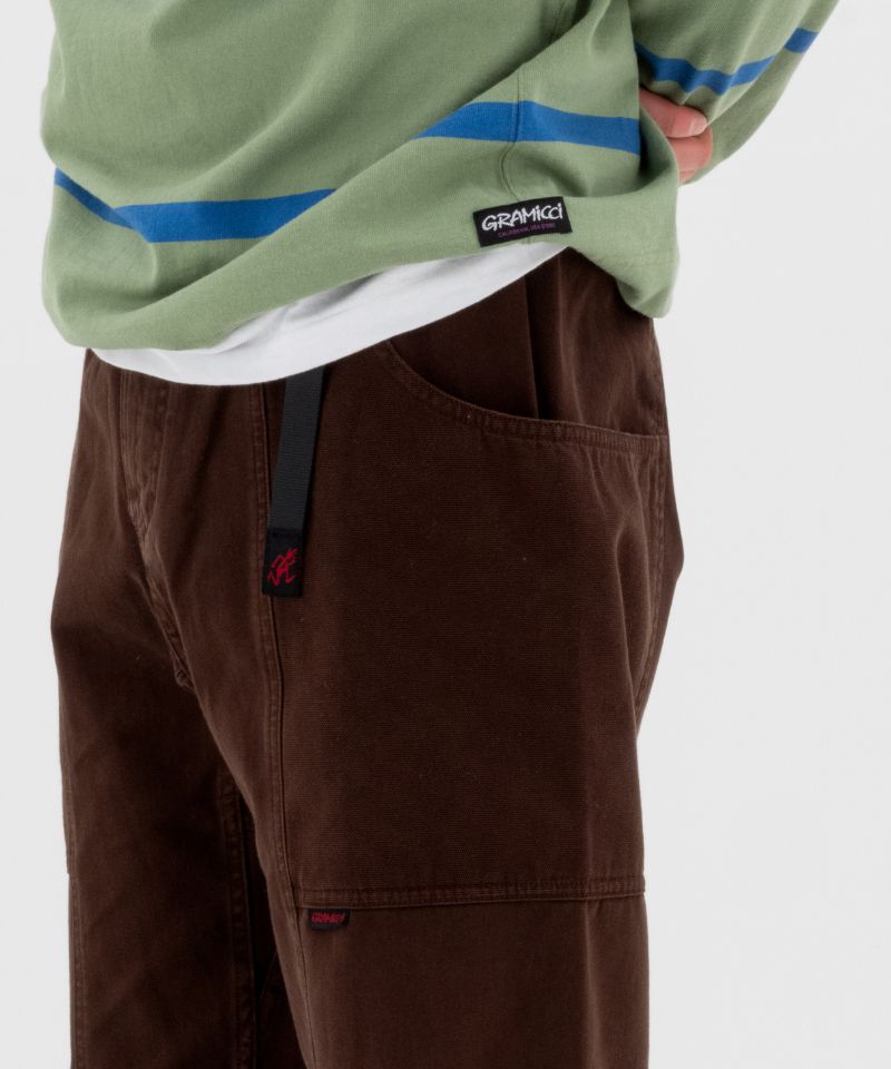 Model wearing a olive and blue stripped Gramicci Gramicci Langdon Rugby Shirt and brown pants on a light-tone background.