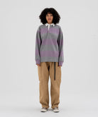 Model wearing beige Gramicci Voyager Pants and a lavender and grey stripped Gramicci Langdon Rugby  Long-Sleeve shirt on a light-tone background.