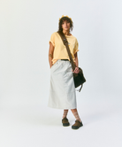 Model wearing a mango colored t-shirt, light gray skirt, amber Hemp Blend Socks, and brown shoes on a light-tone background.