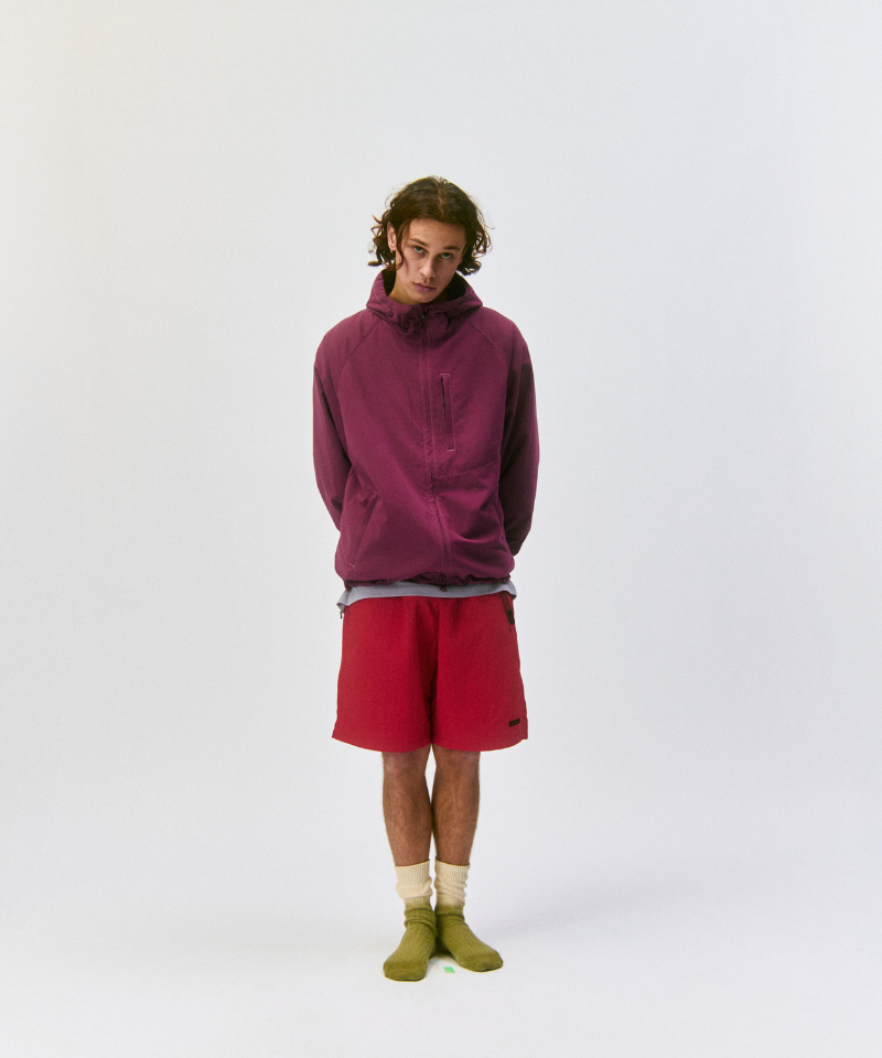 Person wearing a maroon pullover, red shorts, and Cactus colored Gramicci Dip Dye Socks against a light-tone background.