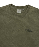 Close-up of an olive green mineral-washed t-shirt with a small black embroidered 'GRAMICCI' logo on the left chest, showing the inner neck label and fabric texture.